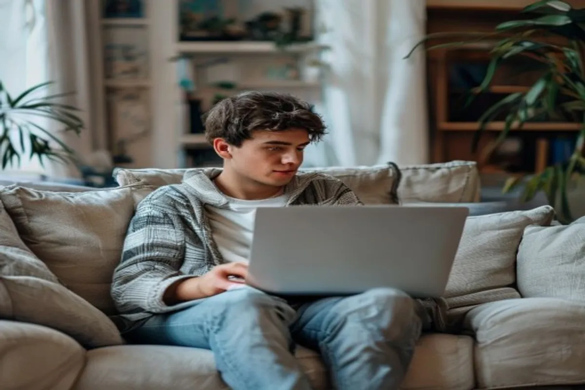 Jovem adulto sentado em sofá usando notebook, sala de estar organizada e tranquila ao fundo, atmosfera de autonomia e praticidade.